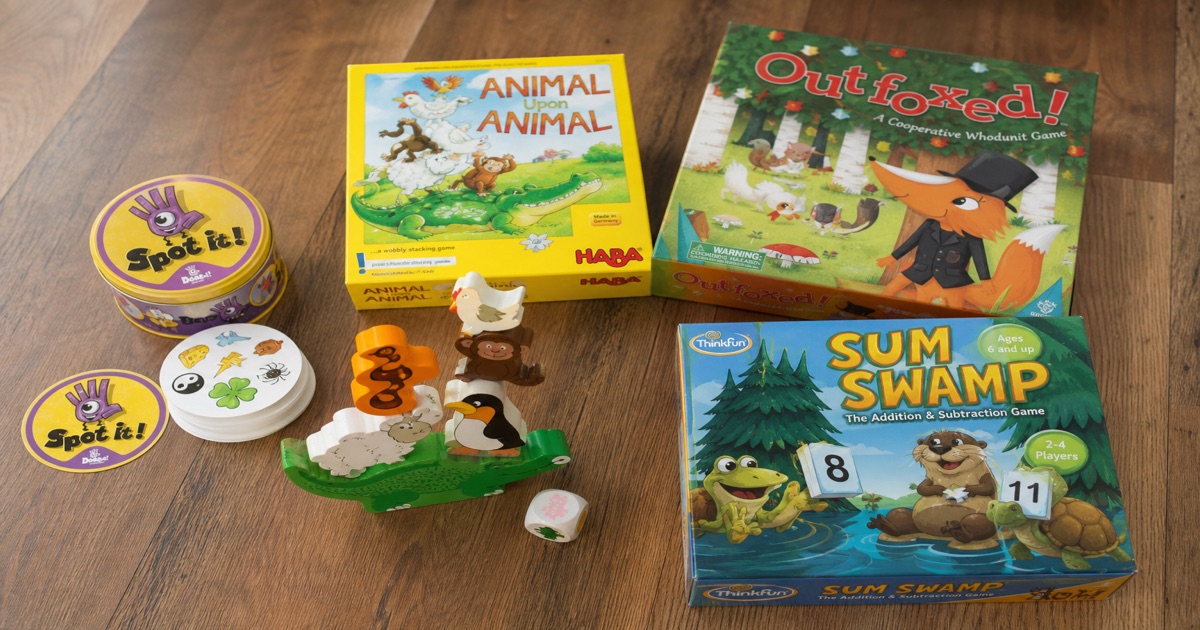 Best educational games for kids that are fun in 2026 — Spot It, Animal Upon Animal, Outfoxed, and Sum Swamp laid out on a wooden floor.
